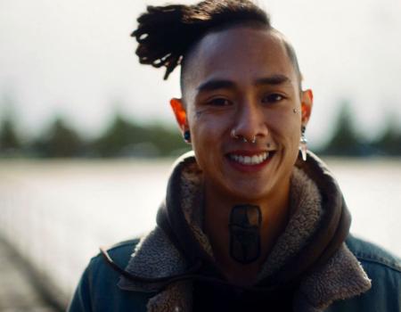 Close up of young man with dreadlocks, tattoos and piercings looking at the camera.